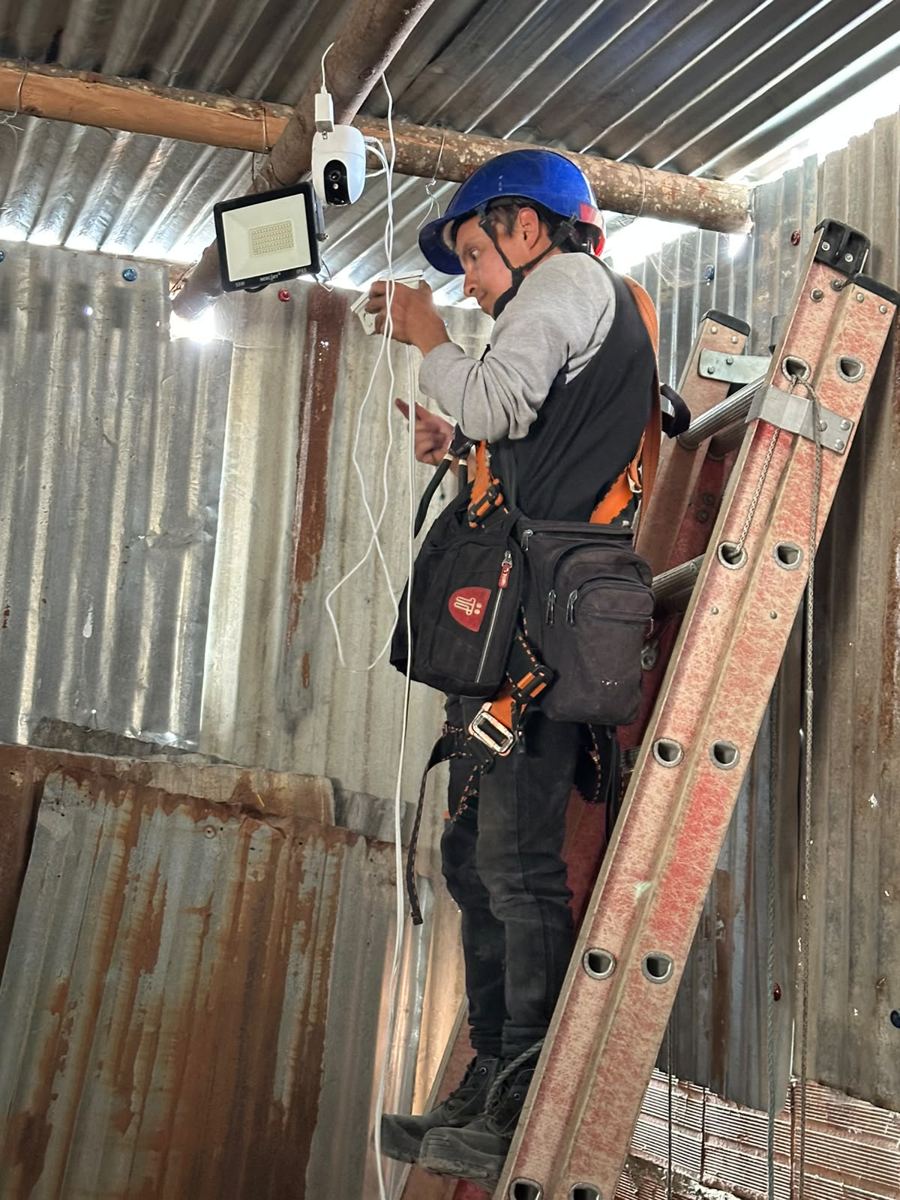 Técnico instalando cámara de seguridad y reflector en techo de zinc