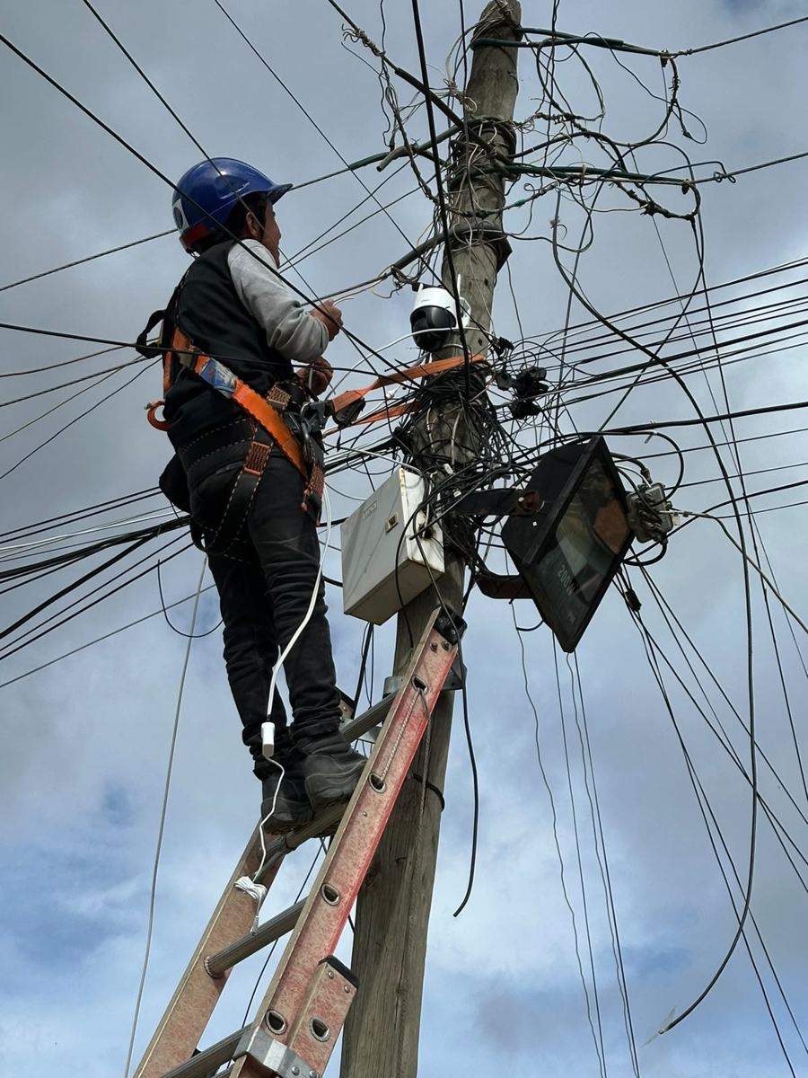 Técnico con arnés instalando cámara y equipos en poste de energía